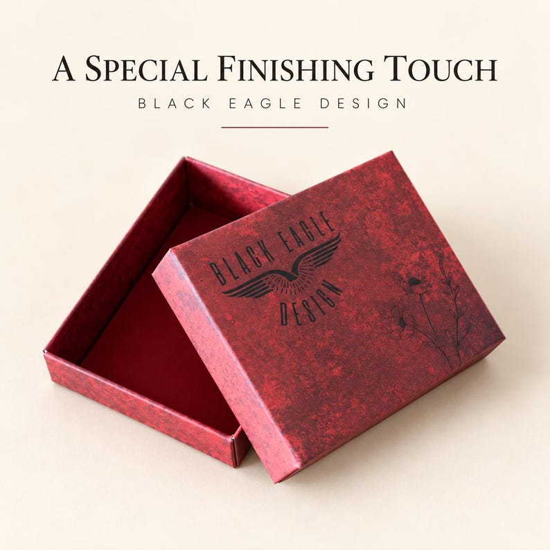 May include: A rectangular red gift box with a textured finish, featuring a black eagle logo and floral line art. The lid is partially open, revealing a solid red interior. The text A SPECIAL FINISHING TOUCH BLACK EAGLE DESIGN is visible.