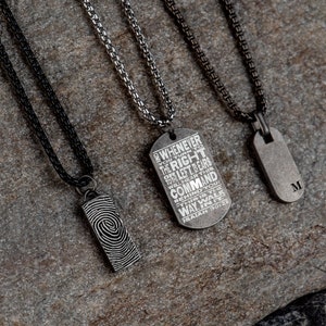 May include: Three silver necklaces with different pendants. The first pendant is a rectangular tag with the text "WHENEVER YOU TURN TO THE RIGHT OR LEFT, YOUR EARS WILL HEAR THIS COMMAND BEHIND YOU: THIS IS THE WAY. WALK IN IT. ISAIAH 30:21". The second pendant is a rectangular tag with a fingerprint design. The third pendant is a rectangular tag with the letter "M" engraved on it.