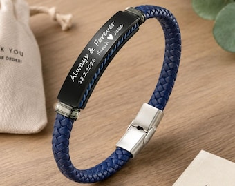 May include: A blue braided leather bracelet with a black metal plate engraved with "Always & Forever" and the names "Sarah" and "Jake" along with the date "12.2.2026". The bracelet has a silver clasp.