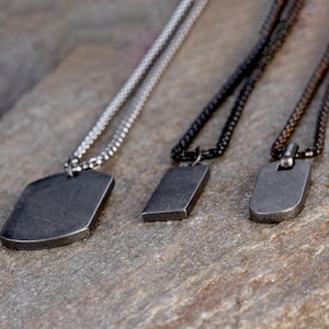 May include: Three silver, black, and brown chain necklaces with rectangular metal pendants. The pendants are all different sizes and have a brushed metal finish.