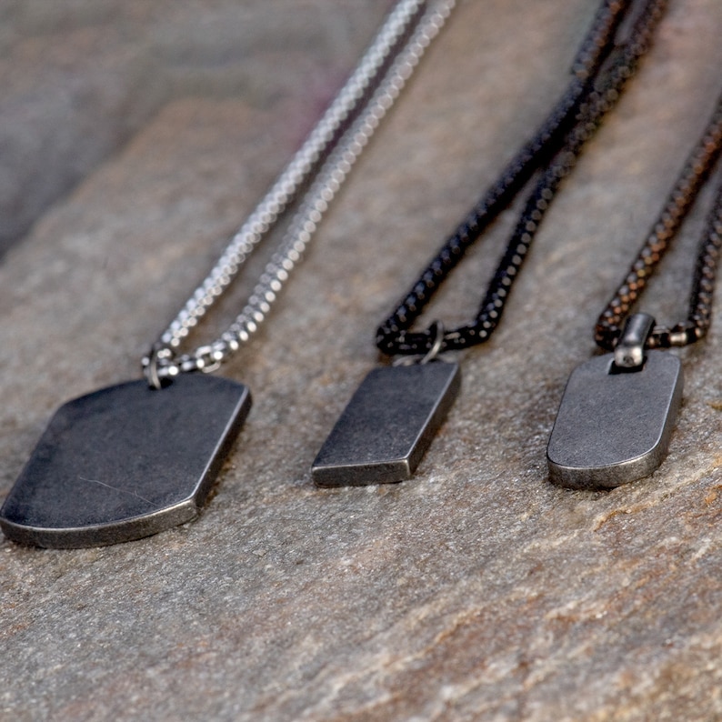 May include: Three silver, black, and brown chain necklaces with rectangular metal pendants. The pendants are all different sizes and have a brushed metal finish.