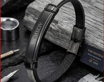May include: A black bracelet with a mesh and leather band. The bracelet has a black metal plate with the Roman numeral MCMXCIV engraved on it. The clasp is stainless steel. A tag reads "Hand Crafted By Erhan Kahraman Est. 2026."