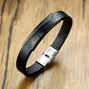 Puede incluir: Pulsera de cuero negro con cierre de plata y texto grabado que dice "27° 57' 09.9" N 82° 43' 26.5" W Sara & Eric".