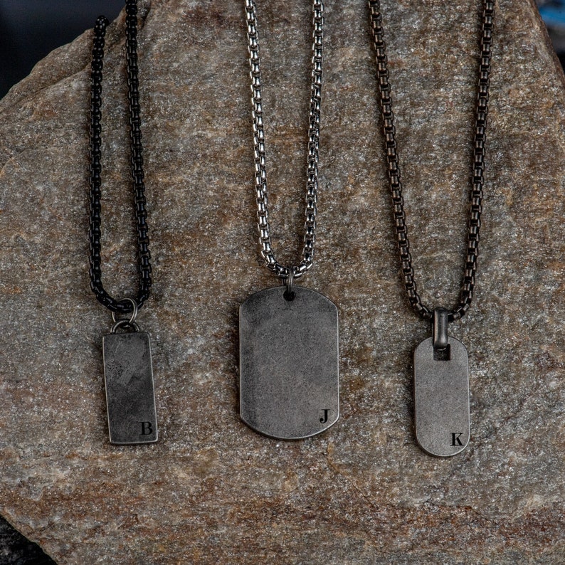 May include: Three silver dog tag necklaces with different chain styles. The tags are engraved with the letters B, J, and K.