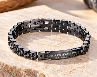 May include: A black metal link bracelet featuring a rectangular plate engraved with the coordinates 34°41'21.4"N 48°67'54.9"W and the Roman numeral date VII.XXVI.MMXXIV. The bracelet has a multi-link chain design with a matte finish.
