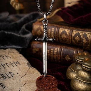 Puede incluir: Collar con colgante de espada plateada. El colgante es una espada en miniatura con empuñadura y hoja detalladas. La hoja tiene grabados números romanos y el nombre "William". La cadena del collar también es plateada.