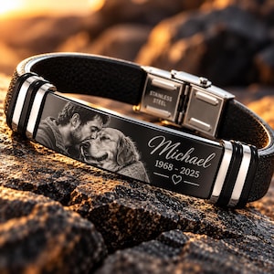 May include: A black leather bracelet with a stainless steel plate featuring an engraved black and white portrait of a person and a dog, the name Michael, the dates 1968-2025, and a heart symbol. The clasp is marked with the text STAINLESS STEEL.
