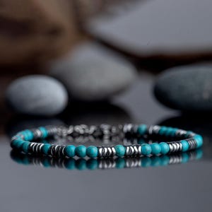 Puede incluir: Un brazalete de cuentas turquesa y plata. El brazalete está hecho con cuentas redondas de turquesa y cuentas espaciadoras de plata.