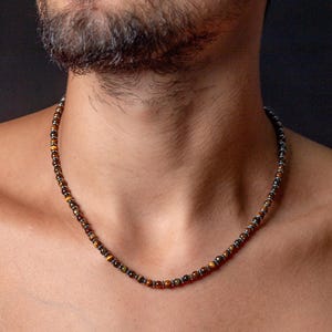 Puede incluir: Un collar de cuentas marrones y doradas con detalles plateados. El collar está hecho de cuentas de ojo de tigre y lo lleva una persona.