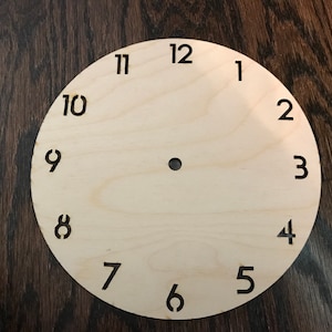 May include: A plain wooden clock face with black numbers 1 through 12.