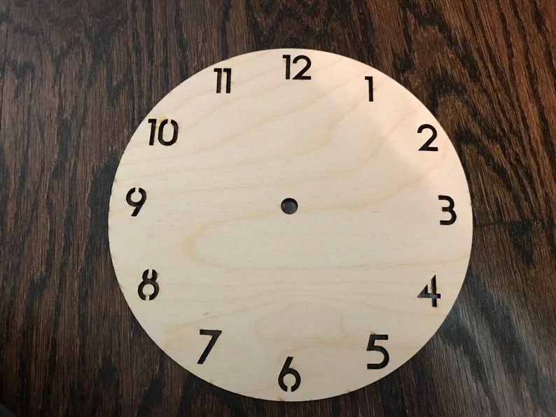 May include: A plain wooden clock face with black numbers 1 through 12.