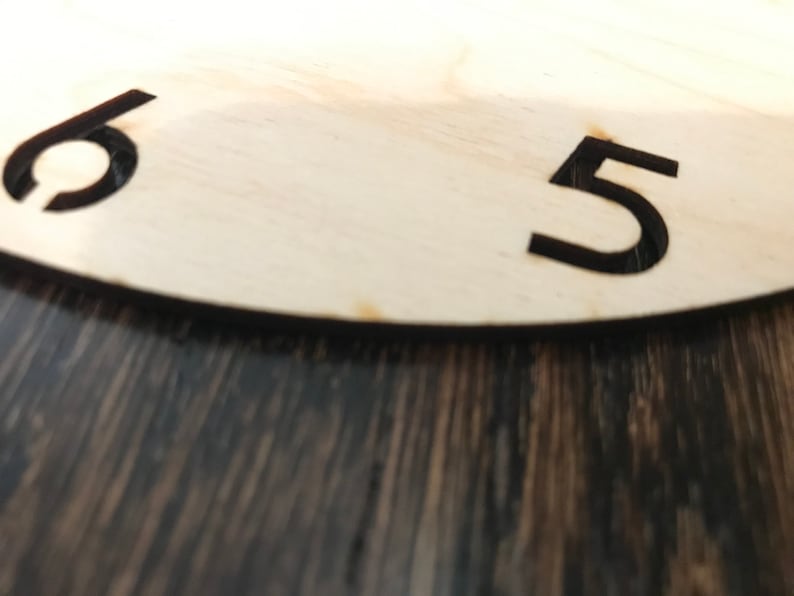 May include: Close-up of a wooden clock face with black numbers 5 and 6.