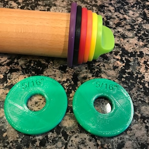 May include: Two green plastic rolling pin rings with a 5/16 inch diameter. The rings are on a granite work surface.