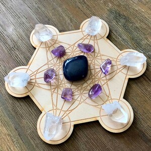 Puede incluir: Una rejilla de madera con un patr&oacute;n geom&eacute;trico, conocida como rejilla de geometr&iacute;a sagrada, con cristales de cuarzo transparente y cristales de amatista colocados en los puntos. Una piedra de obsidiana negra se coloca en el centro de la rejilla.