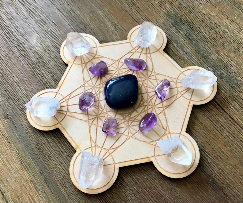 Puede incluir: Una rejilla de madera con un patr&oacute;n geom&eacute;trico, conocida como rejilla de geometr&iacute;a sagrada, con cristales de cuarzo transparente y cristales de amatista colocados en los puntos. Una piedra de obsidiana negra se coloca en el centro de la rejilla.