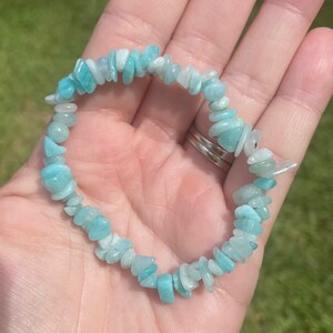 May include: A light blue gemstone bracelet made of small, irregular shaped chips of aquamarine. The bracelet is strung on elastic cord and is approximately 7 inches in length.