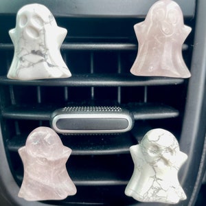 May include: Four ghost-shaped car air fresheners. Two are white with gray marbling and two are pink. The air fresheners are hanging from the air vents of a car.