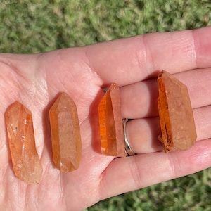 May include: Four orange crystal points with a pointed tip and a flat base. The crystals are translucent and have a slight shimmer.
