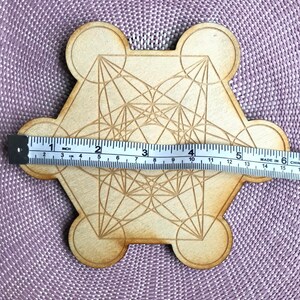 Puede incluir: Un mandala de madera con forma hexagonal con un dise&ntilde;o geom&eacute;trico, que mide 15 cm de di&aacute;metro. El mandala est&aacute; hecho de madera marr&oacute;n claro y tiene un acabado natural.