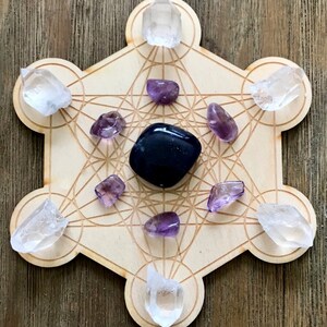 Puede incluir: Una rejilla de madera con un patr&oacute;n geom&eacute;trico, conocida como rejilla de geometr&iacute;a sagrada, con cristales de cuarzo transparente y amatista colocados en los puntos. Un cristal de obsidiana negra se coloca en el centro.