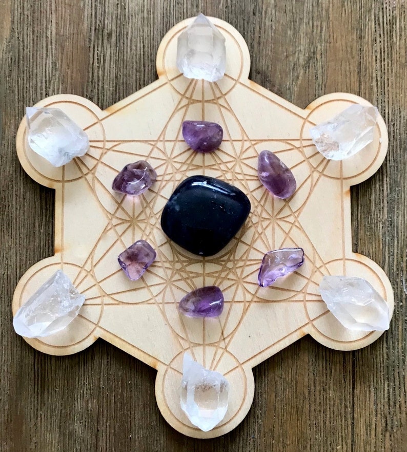 Puede incluir: Una rejilla de madera con un patr&oacute;n geom&eacute;trico, conocida como rejilla de geometr&iacute;a sagrada, con cristales de cuarzo transparente y amatista colocados en los puntos. Un cristal de obsidiana negra se coloca en el centro.