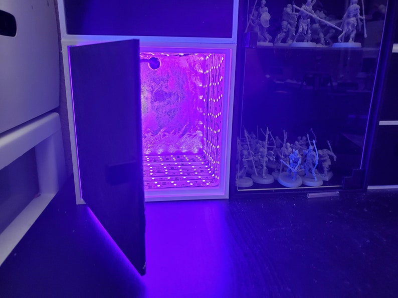 May include: A white cube with a purple light inside and a black door that is open. The cube is sitting on a black surface.