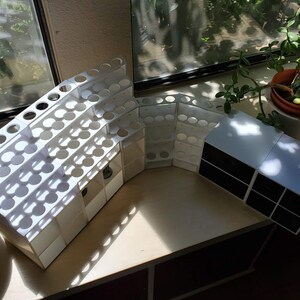May include: White plastic organizer with multiple compartments for storing small items, such as paint tubes or makeup brushes. The organizer is curved and has a modern design. A smaller white organizer with black compartments is also visible in the image.