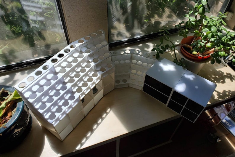 May include: White plastic organizer with multiple compartments for storing small items, such as paint tubes or makeup brushes. The organizer is curved and has a modern design. A smaller white organizer with black compartments is also visible in the image.