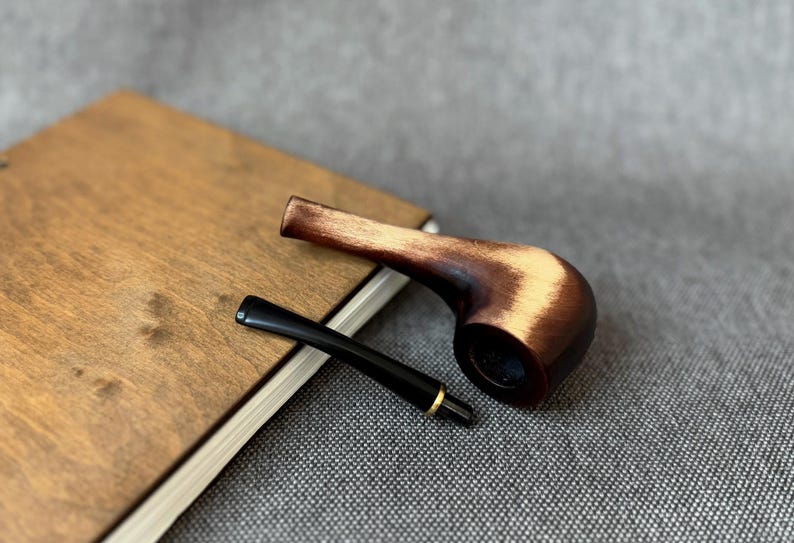 May include: A tobacco pipe with a polished dark brown wooden bowl featuring lighter wood grain highlights and a detachable black stem with a thin gold-coloured metal ring at the connection point.