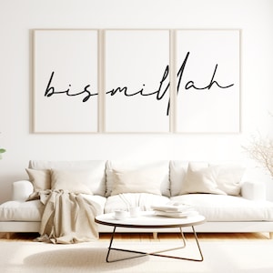 Puede incluir: Tres impresiones enmarcadas con la palabra "bismillah" escrita en caligrafía negra sobre fondo blanco. Las impresiones están colgadas en una pared blanca sobre un sofá blanco con cojines y una manta beige.