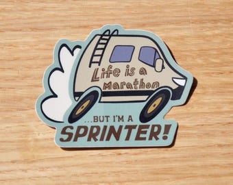 May include: A sticker featuring a cartoon van with the text "Life is a Marathon...BUT I'M A SPRINTER!". The van is beige with blue windows and a ladder on top. The sticker has a light blue border and is on a wooden surface.