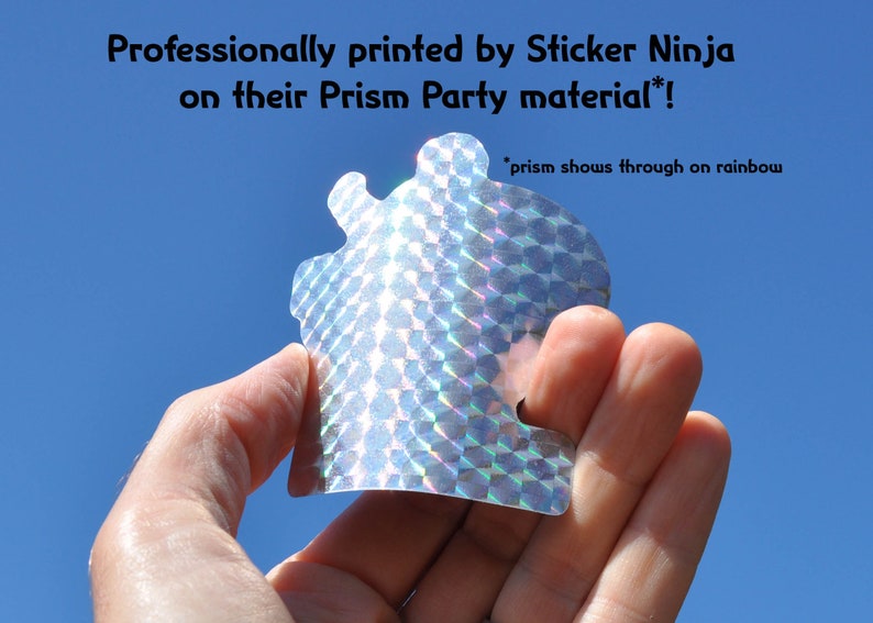 K&ouml;nnte beinhalten: Ein silberner holografischer Aufkleber mit einem geometrischen Muster. Der Aufkleber wird in einer Hand vor einem blauen Himmel gehalten. Der Text "Professionally printed by Sticker Ninja on their Prism Party material!" befindet sich &uuml;ber dem Aufkleber. Der Text "*prism shows through on rainbow" befindet sich unter dem Aufkleber.