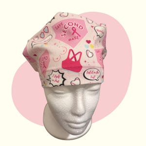 May include: A pink and white patterned surgical scrub cap. The cap features a repeating pattern of pink ribbons, hearts, and the text "Save Second Base" and "I fight in Pink". A pink sports bra graphic is also visible.
