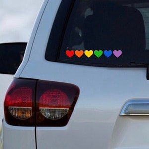 May include: A white car with a rainbow heart sticker on the back window. The sticker is made up of seven hearts, each a different color of the rainbow.