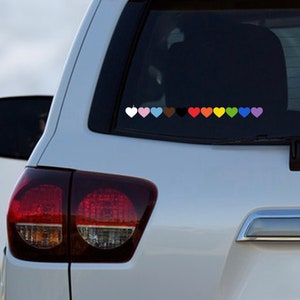 May include: A white car with a row of colorful heart stickers on the back window. The hearts are in the colors white, pink, light blue, brown, black, red, orange, yellow, green, blue, and purple.