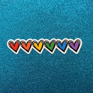 Puede incluir: Una fila de seis corazones de colores arco&iacute;ris con contornos negros. Los corazones est&aacute;n dispuestos en l&iacute;nea de izquierda a derecha, con los colores rojo, naranja, amarillo, verde, azul y morado.