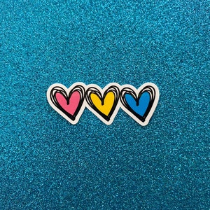 Puede incluir: Tres corazones dibujados a mano en fila, con contornos rosa, amarillo y azul. Los corazones est&aacute;n sobre un fondo azul brillante.