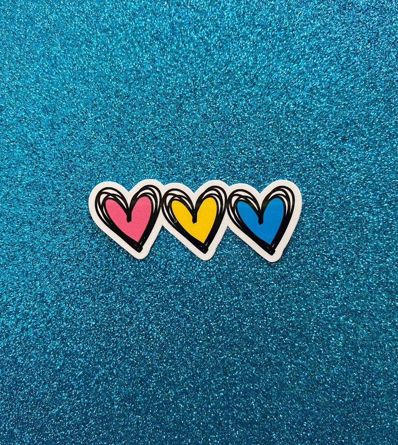 Puede incluir: Tres corazones dibujados a mano en fila, con contornos rosa, amarillo y azul. Los corazones est&aacute;n sobre un fondo azul brillante.