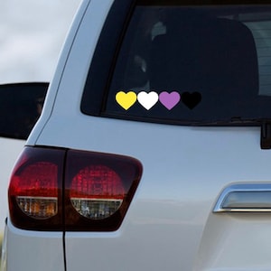 May include: A white car with a black and white heart sticker on the back window. The sticker has four hearts in a row, yellow, white, purple, and black.