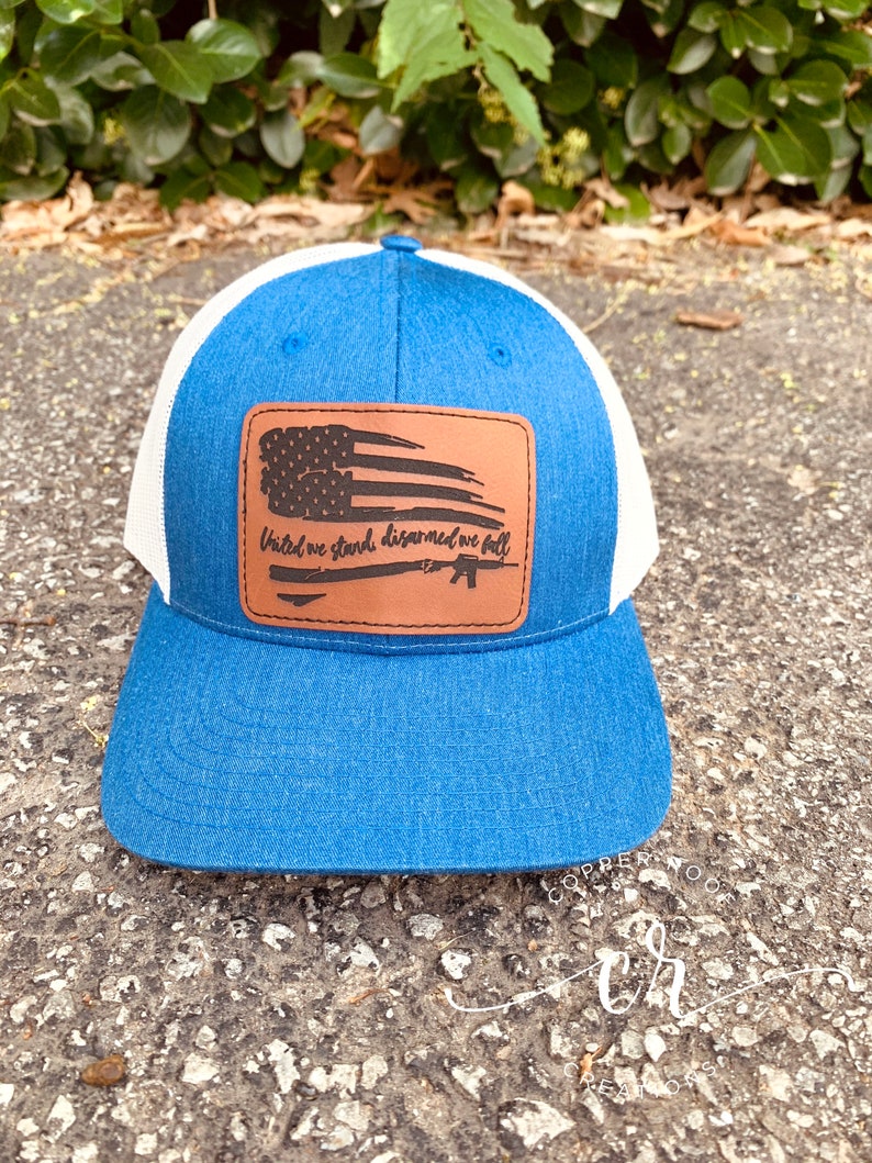 May include: A blue and white trucker hat with a brown leather patch featuring a distressed American flag and the text "United we stand, disarmed we fall".