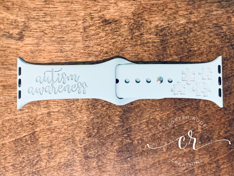 May include: Light blue Apple Watch band with the text "autism awareness" and puzzle pieces engraved on the band.