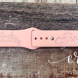 May include: A pink Apple Watch band with the text "Think differently" and a pattern of puzzle pieces. The band is made by Copper Roof Creations.