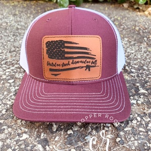 May include: A maroon and white trucker hat with a brown leather patch featuring a distressed American flag and the text "United we stand, disarmed we fall".