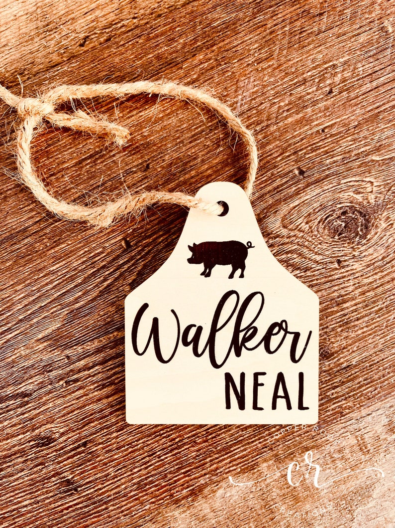 May include: A white wooden tag with a black pig silhouette, a crescent moon, and the text "Walker Neal". The tag is attached to a piece of twine.