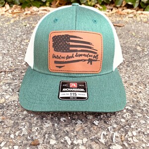 May include: A green and white trucker hat with a brown leather patch featuring a distressed American flag and the text "United we stand disarmed we fall". The patch also includes a silhouette of a rifle. The hat has a Richardson brand label.