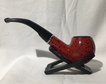 May include: A red and black tobacco pipe with a black stand. The pipe has a speckled red finish with black spots.