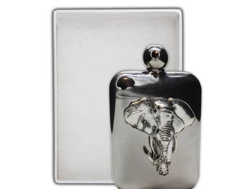 May include: A silver-colored flask with an embossed elephant design. The flask has a rounded top with a small, round stopper. The flask is rectangular with rounded corners and is next to a white box.