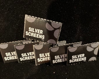 May include: Close-up of a stack of black and white packaging for Silver Screens. The packaging has a white circle with a pattern of small white dots. The text "Silver Screens" is printed in white on the packaging.
