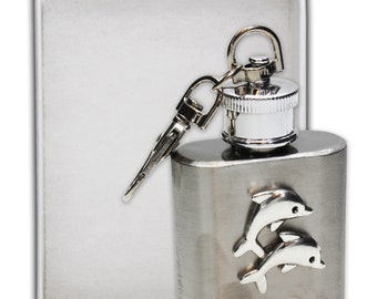 May include: A silver flask with a dolphin design and a silver cap and keychain. The flask is in a white box.
