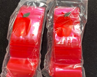 May include: Two packages of red plastic zipper bags with an apple logo and the text "TM" on each bag. The bags are stacked and sealed in clear plastic.